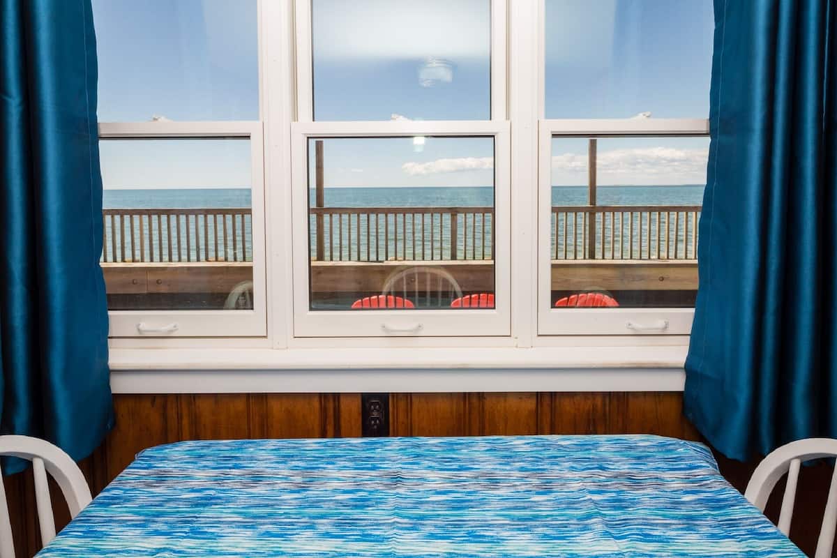 Huoneessa on sänky, ikkunasta avautuu näkymä merelle ja ulkona on puinen terassi.