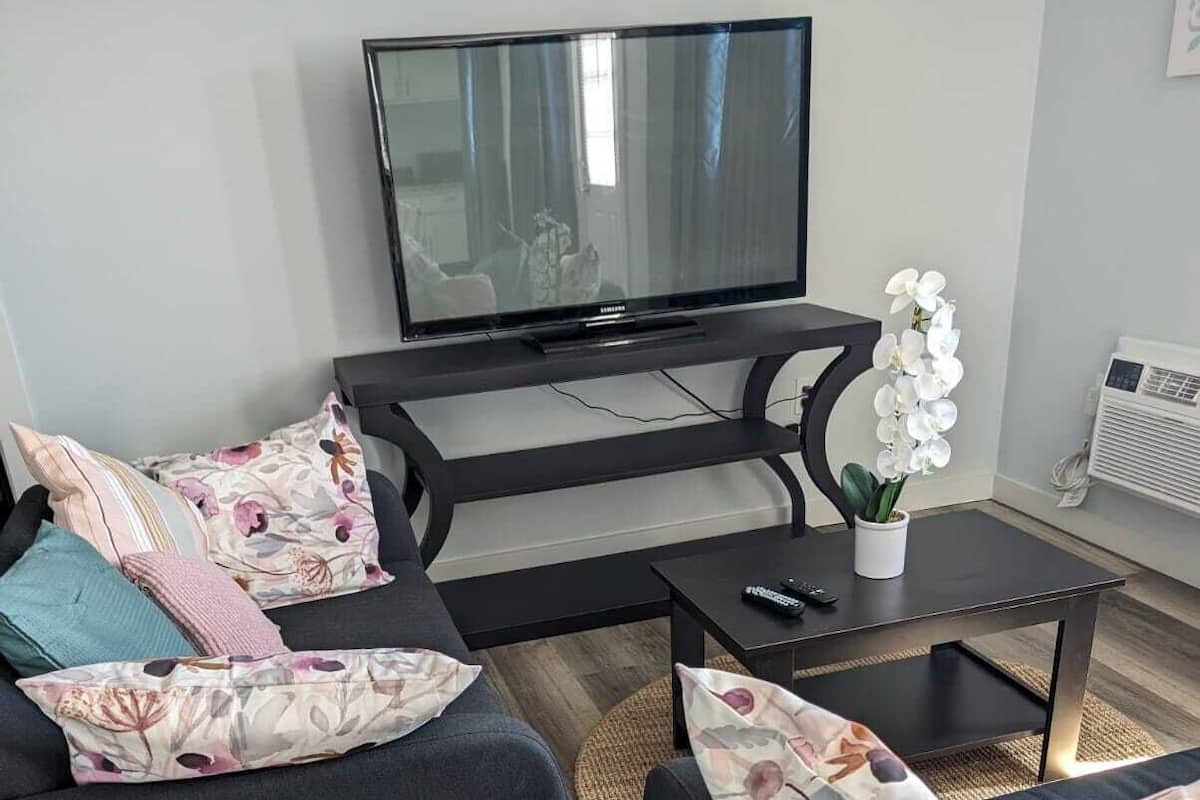 Moderni olohuone, jossa on litteänäyttöinen televisio, kaksi mustaa sohvaa, joissa on kukalliset koristetyynyt, pieni sohvapöytä ja ruukussa oleva orkidea.