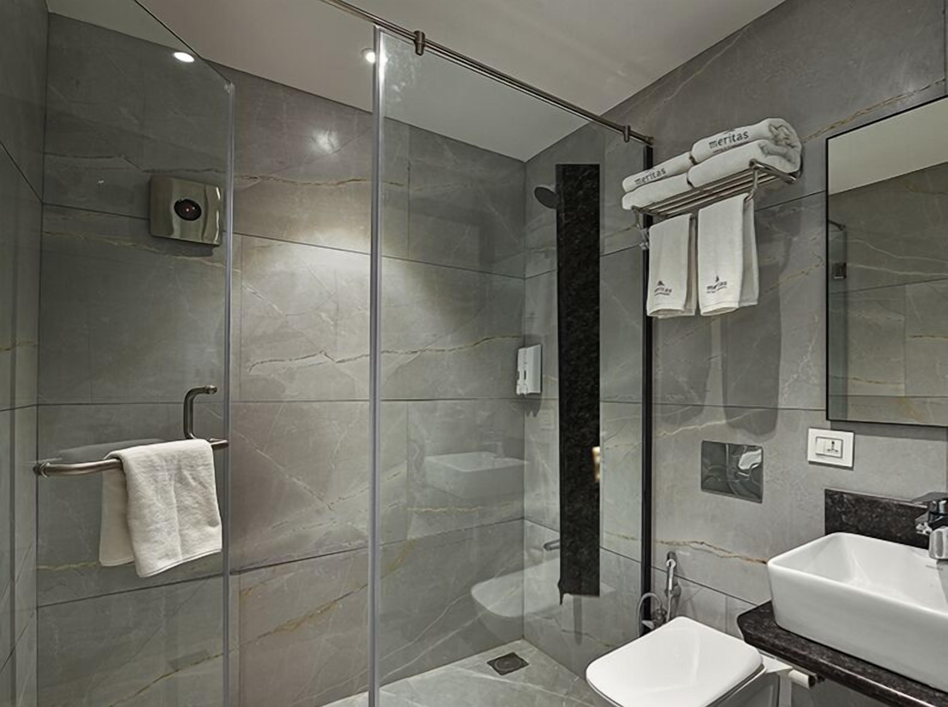 Un baño moderno con cabina de ducha de vidrio, un lavamanos blanco y un perchero para toallas.