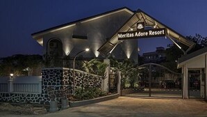 Exterior del Meritas Adore Resort, con un muro de piedra, entrada protegida por un portón y un letrero sobre el edificio principal.