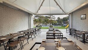 Un amplio comedor al aire libre con varias mesas y sillas, una zona cubierta y vistas a un parque infantil y zonas verdes.