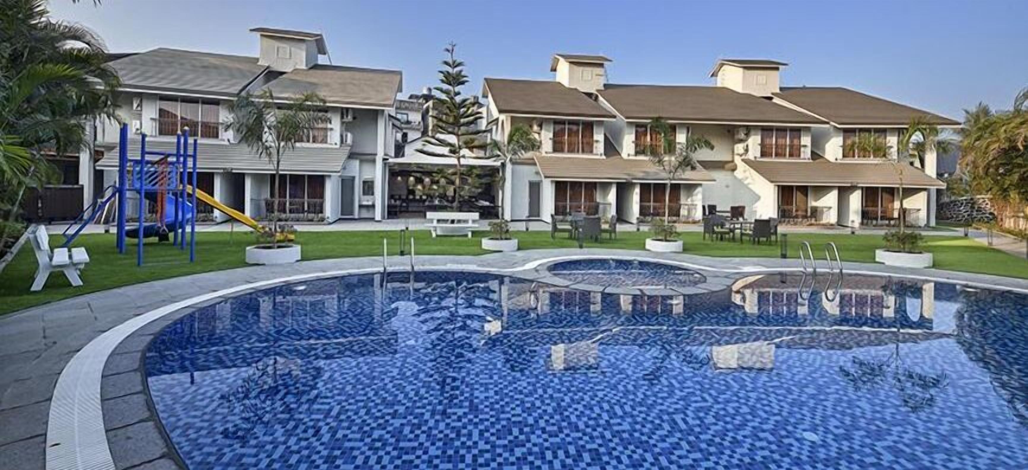 Un hotel moderno con piscina, mobiliario de exterior y parque infantil.