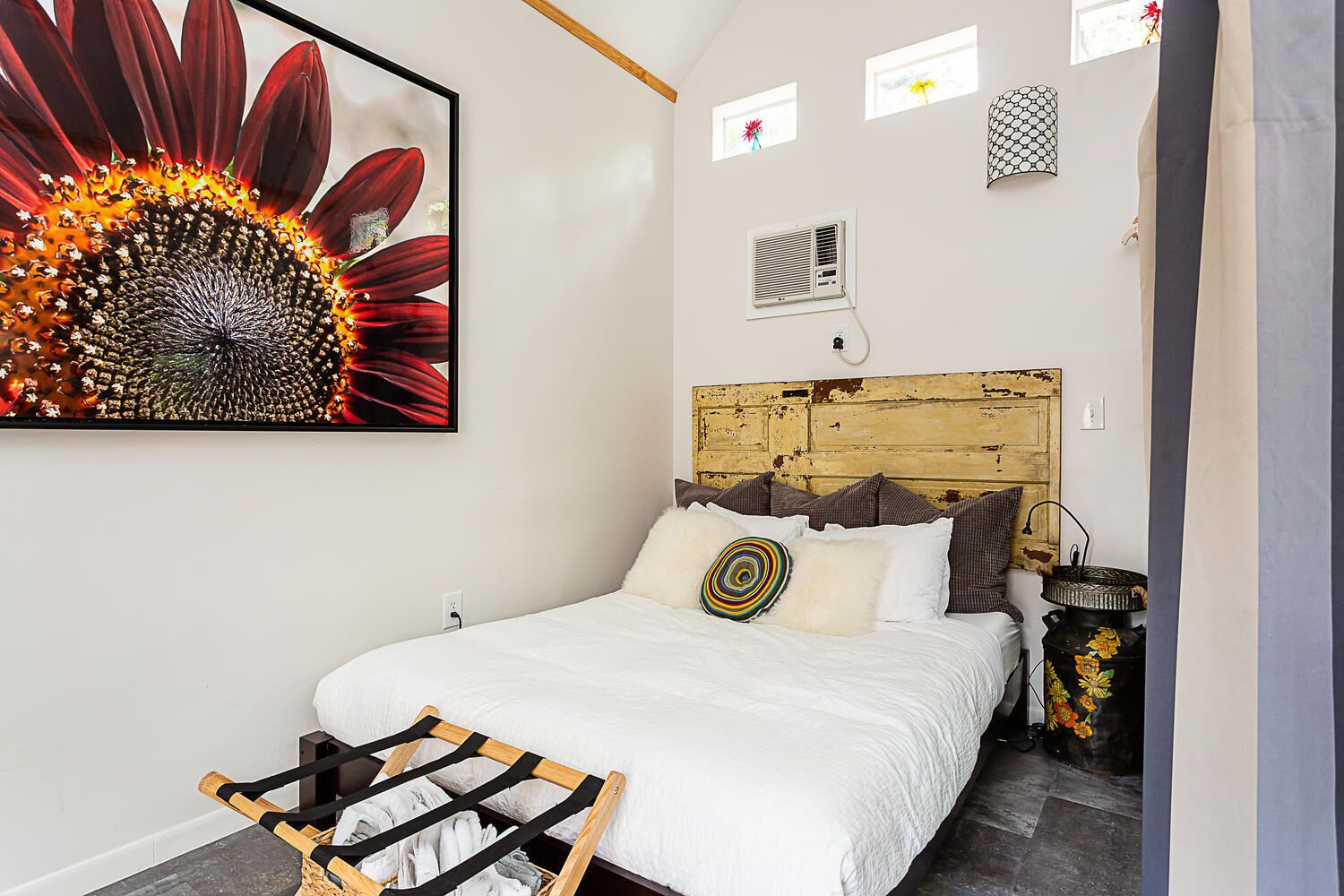 A bedroom with a wooden headboard, white bedding, and a large floral artwork on the wall.