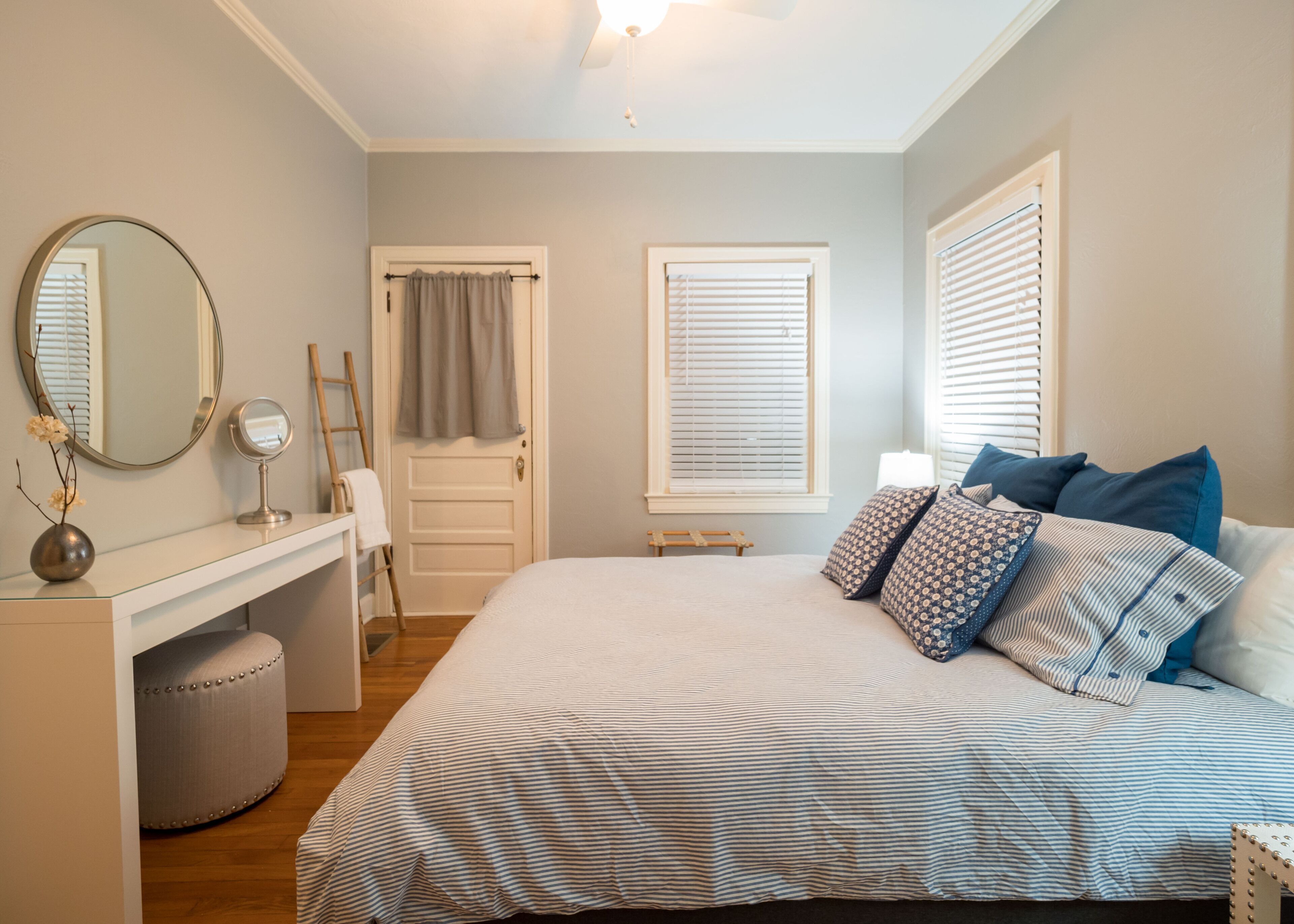 A bedroom with a bed, a vanity with a mirror, a dresser, and a window with blinds.