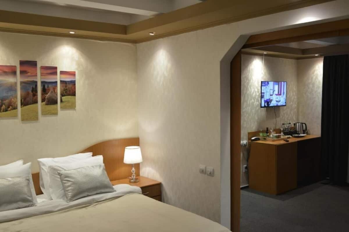 Quarto de hotel com uma cama, uma escrivaninha, uma televisão e uma parede com três quadros.