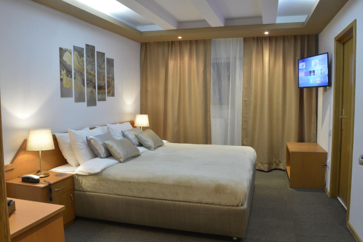 Quarto de hotel com uma cama grande, abajures, televisão de tela plana e uma janela com cortinas.