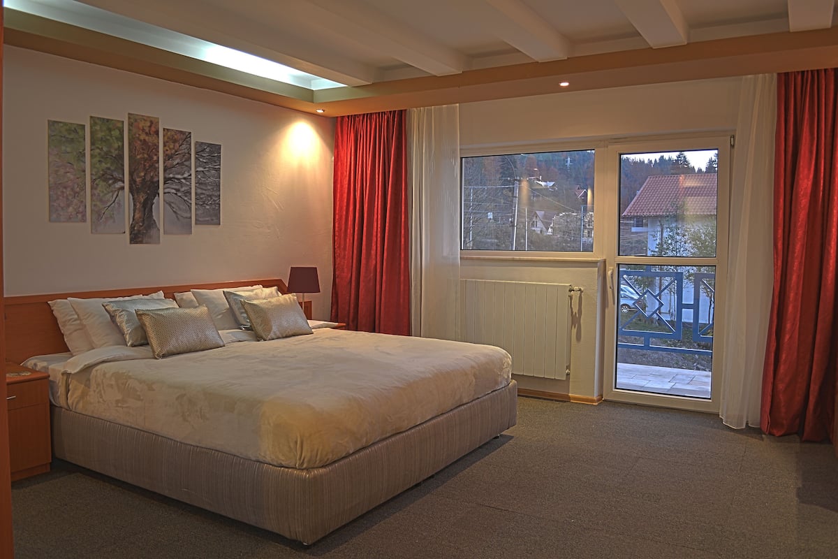 Um quarto com uma cama grande, uma mesa de cabeceira, uma janela com cortinas e um radiador.