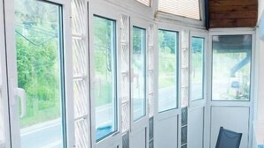 A covered porch with large windows, a wooden table, and two chairs. - Alimar (Predeal)