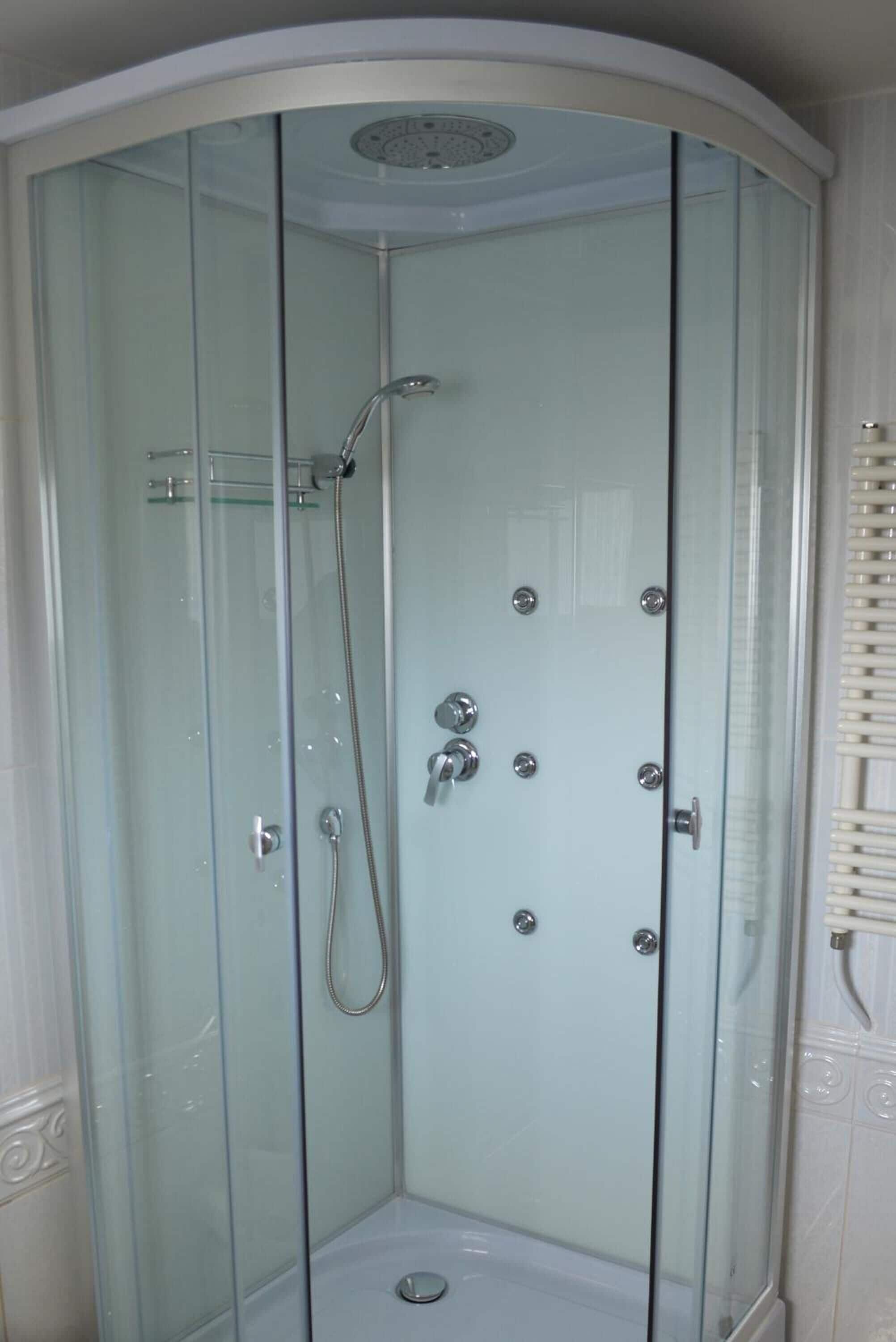 A glass-enclosed shower stall with a handheld showerhead and a wall-mounted faucet.