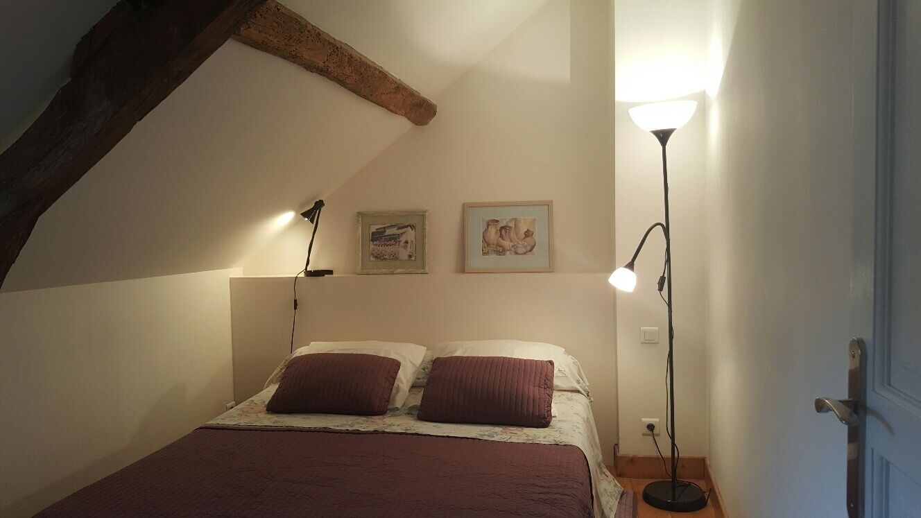 A bedroom with a sloped ceiling, a bed with a red blanket, two bedside lamps, and two framed pictures on the wall.