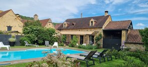 A pool area with lounge chairs, a stone building, and a garden with flowers. - Maison de Noëmie near Sarlat, heated swimming pool from mid-May to the end of September (Daglan)