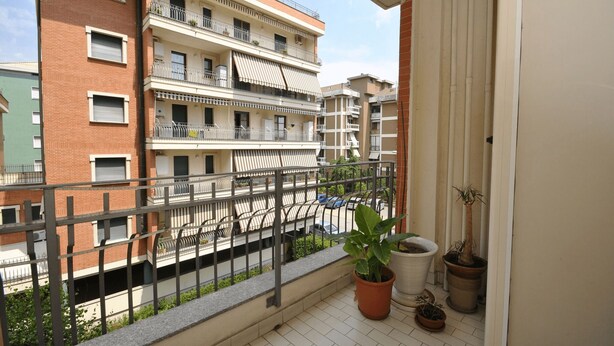 A balcony with potted plants, a metal railing, and a view of a multi-story building with balconies. - Chicco Apartment Light (Vercelli)
