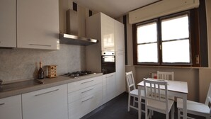 A modern kitchen with white cabinets, a gas stove, and a window with blinds. - Chicco Apartment Light (Vercelli)