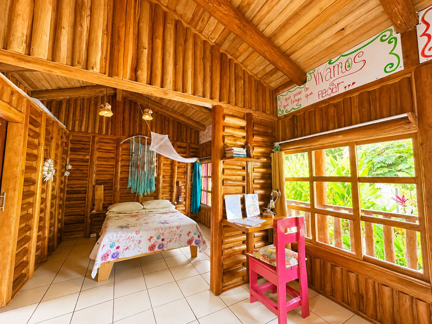 L’intérieur d’une cabane en bois, avec un lit, un bureau, une chaise et de grandes fenêtres.