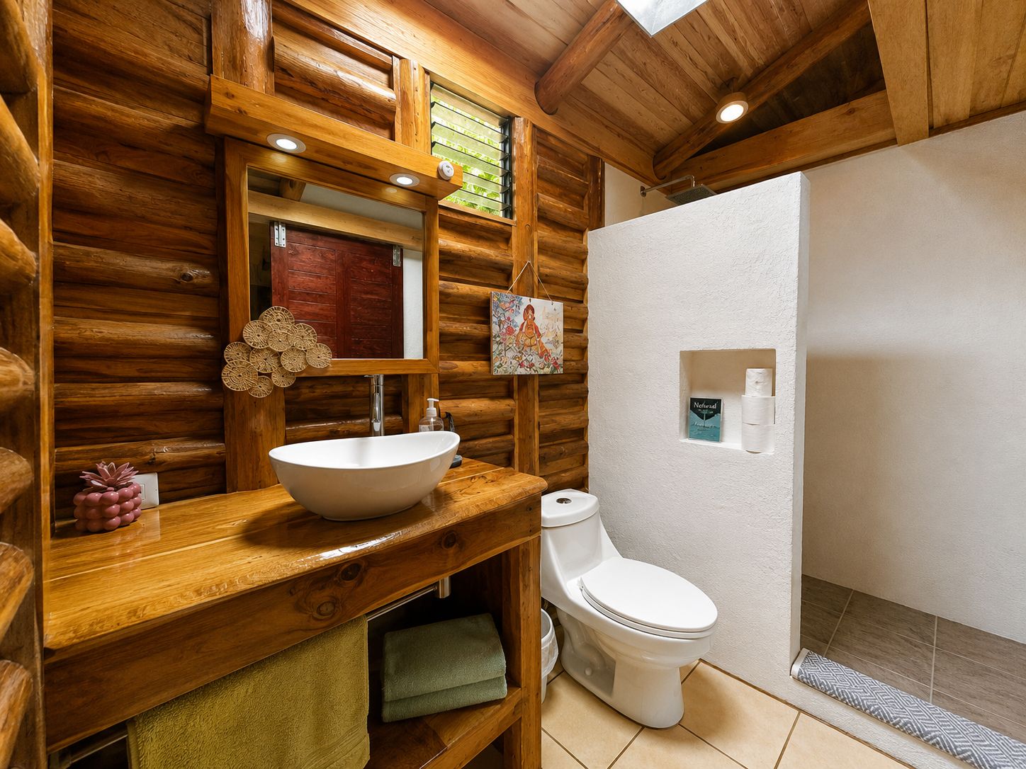 Baño de cabaña de madera con tocador de madera, un lavamanos blanco, un inodoro y zona de ducha.