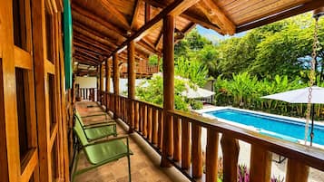 Un balcón de madera con piscina, rodeado de exuberante vegetación.