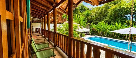 A wooden balcony with a pool, surrounded by lush greenery.