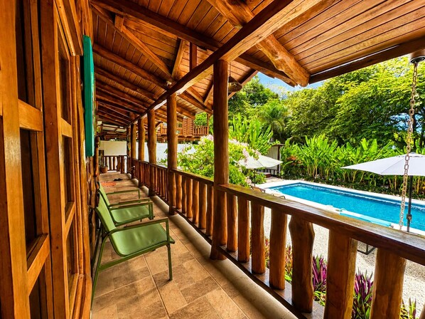 Un balcón de madera con piscina, rodeado de exuberante vegetación.