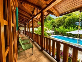Un balcón de madera con piscina, rodeado de exuberante vegetación.