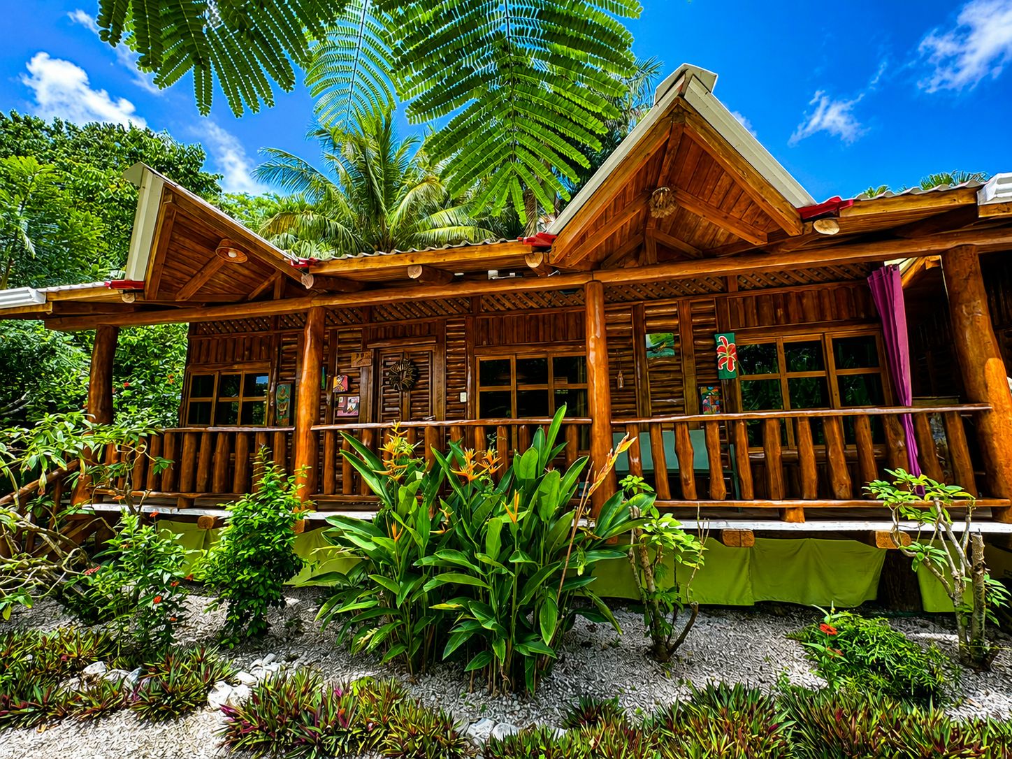 A wooden cabin with a porch, surrounded by tropical vegetation.