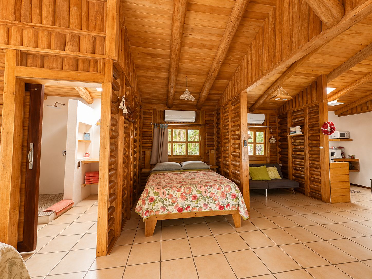 A log cabin room with a bed, a sofa, a small table, and a window with curtains.