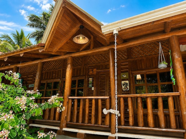 A wooden cabin with a porch, large windows, and a hanging planter. - Cabañas Lamaite (Sámara)