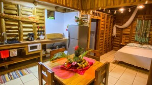 Interior acogedor de una cabaña con una mesa de comedor de madera, sillas, una zona de cocina con refrigerador y una cama con dosel.
