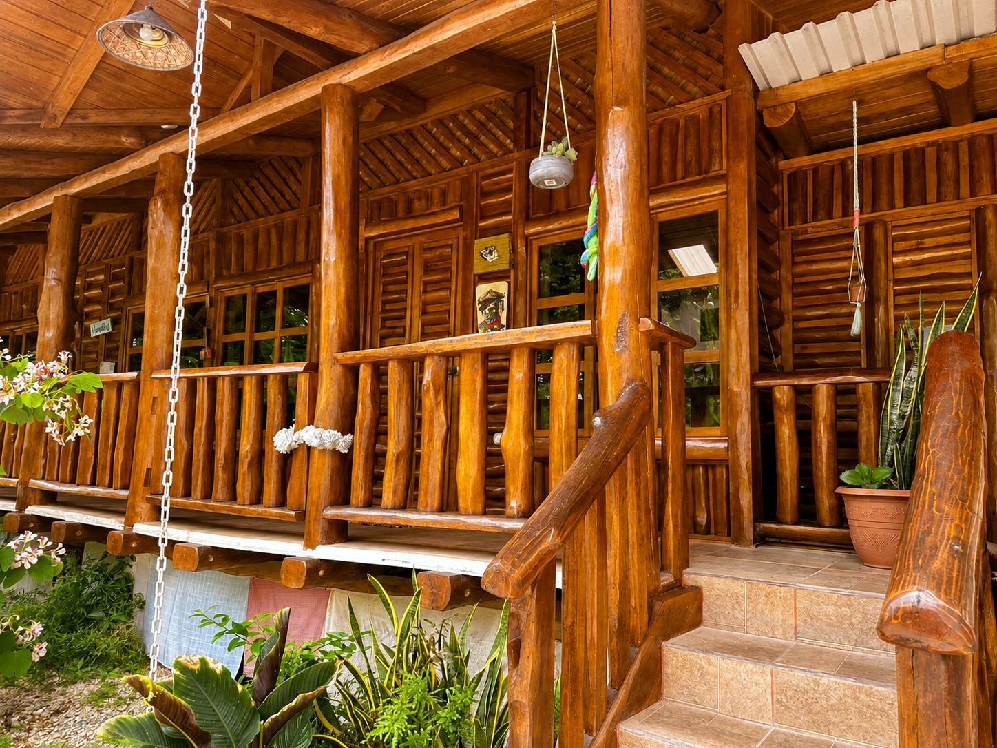 A wooden porch with a staircase, potted plants, and hanging light fixtures.