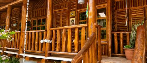 A wooden porch with a staircase, potted plants, and hanging light fixtures.