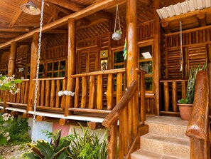 Un porche de madera con escaleras, plantas en macetas y lámparas colgantes.