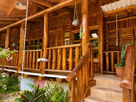 Un porche de madera con escaleras, plantas en macetas y lámparas colgantes.