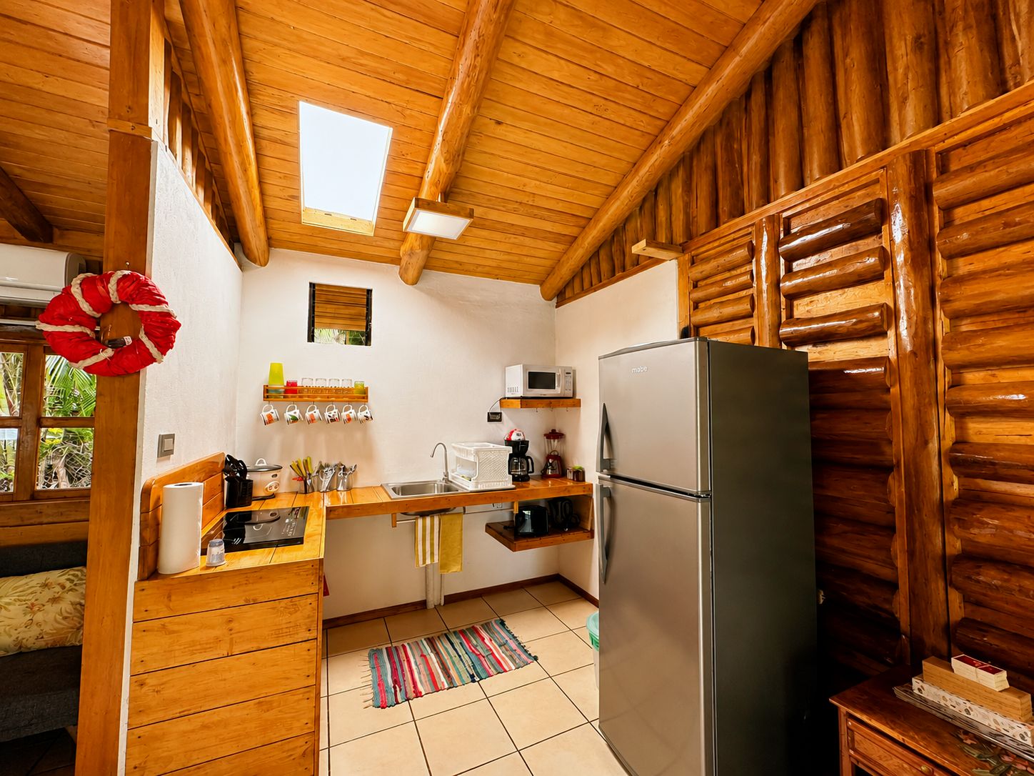 Una cocina compacta con paredes de madera, un refrigerador de acero inoxidable y un ventanal.
