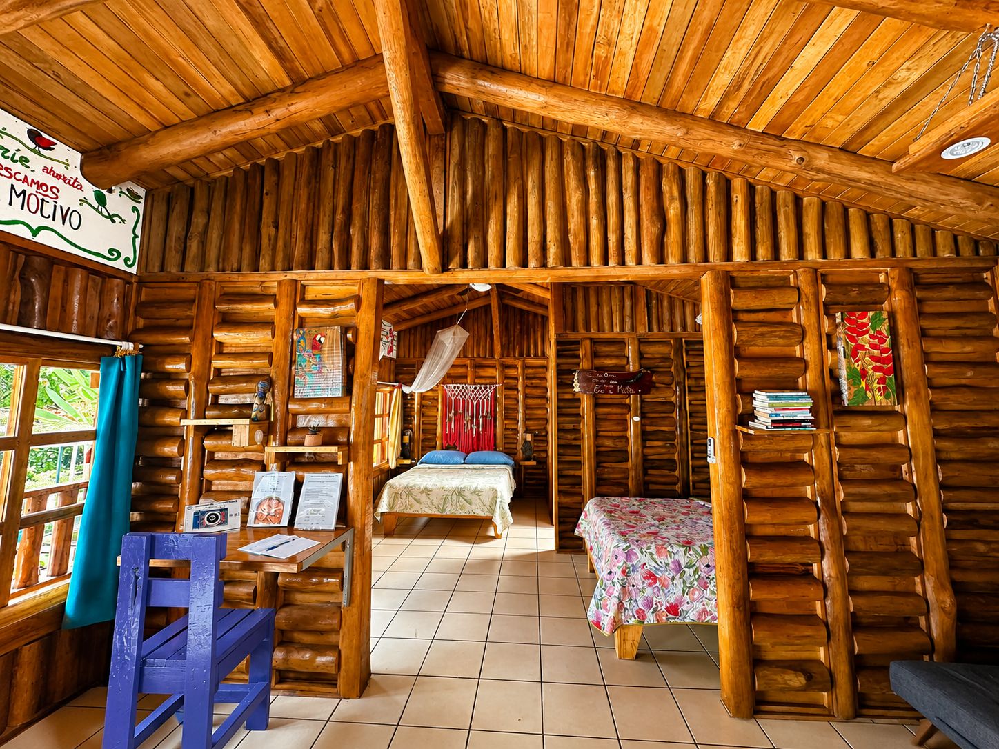 Una cabaña rústica de troncos con una cama, una mesa con un menú y un sillón colgante.