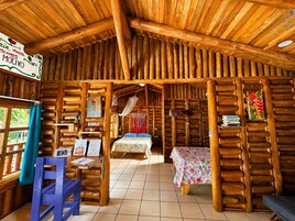 Una cabaña rústica de troncos con una cama, una mesa con un menú y un sillón colgante.