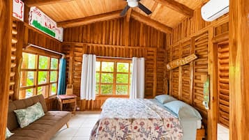 Habitación de cabaña de madera con cama, sofá, ventilador de techo y ventana con cortinas.