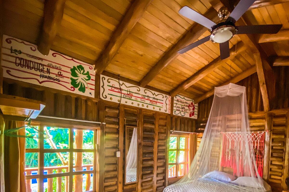 A rustic wooden room with a bed under a canopy, a ceiling fan, and a sign with text.