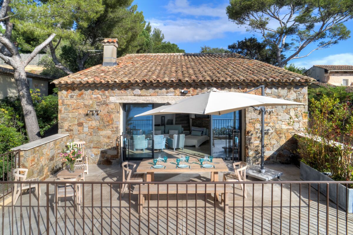 A stone house with a tiled roof, a glass-enclosed patio with outdoor furniture, and a view of the surrounding trees.