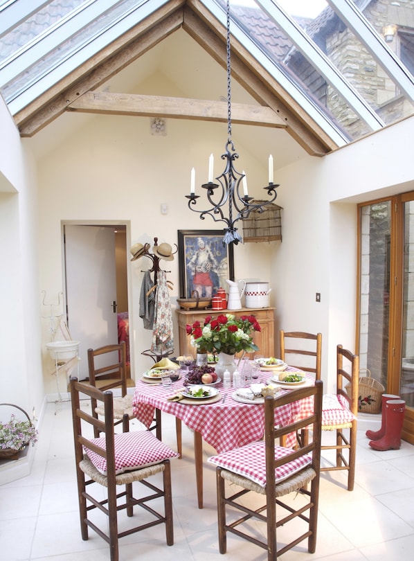 A dining area with a checkered tablecloth, wooden chairs, a chandelier, and a view through a skylight.