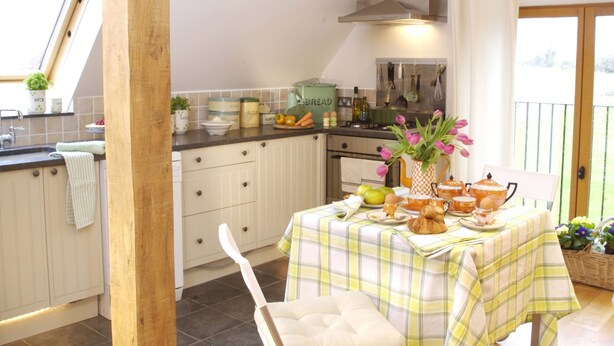 A kitchen with a dining table set for breakfast, a window with a view, and a wooden beam structure. - Castle Combe - the prettiest Cotswold village near Bath / 6 bedrooms ensuite (Castle Combe)