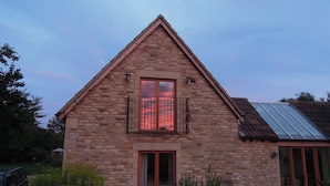 A stone building with a triangular roof, a balcony with metal railings, and a window with a curtain. - Castle Combe - the prettiest Cotswold village near Bath / 6 bedrooms ensuite (Castle Combe)
