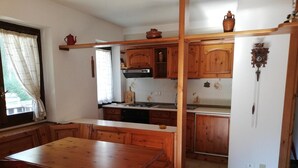 A kitchen with wooden cabinets, a wooden dining table, and a window with curtains. - MORGEX 923 _Monte Bianco_Valdigne (Morgex)