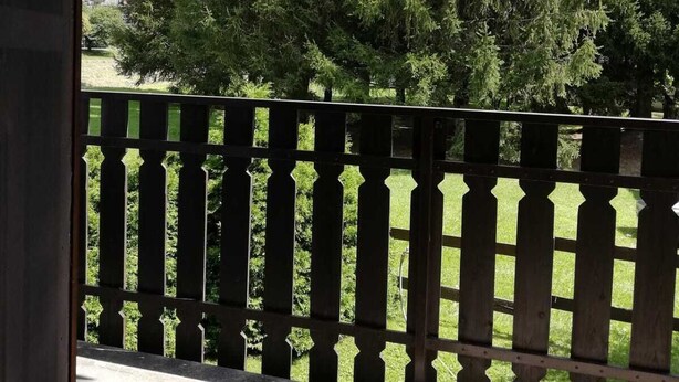 A balcony with a wooden railing overlooking a grassy area and a dense forest. - MORGEX 923 _Monte Bianco_Valdigne (Morgex)