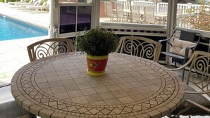 Un porche cubierto con vista a la piscina, una mesa redonda con sillas y una planta en maceta.