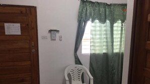 A small room with a wooden door, a white plastic chair, a green curtain, and a tiled floor. - Matus Guest House (San Ignacio)