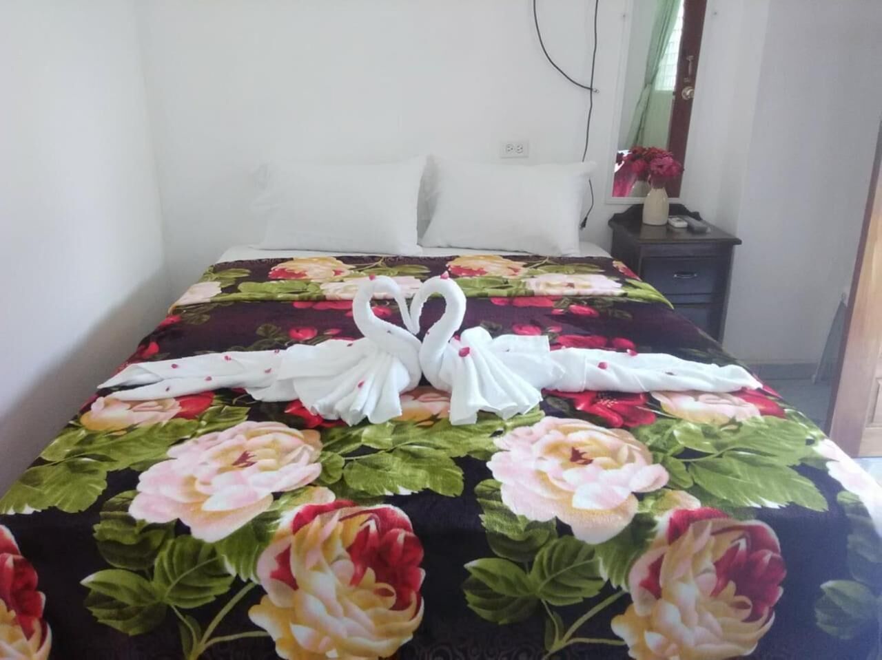 A neatly made bed with a floral bedspread and two white swan-shaped towels.