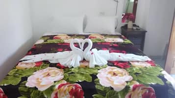 A neatly made bed with a floral bedspread and two white swan-shaped towels.