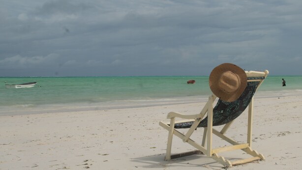Una silla de playa con un sombrero de paja sobre arena fina y agua turquesa.