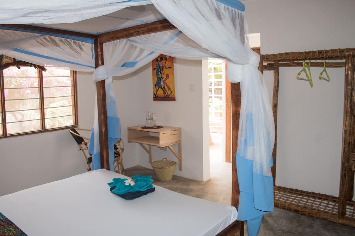 A room with a bed, a small wooden table, a basket, and a window with a view.