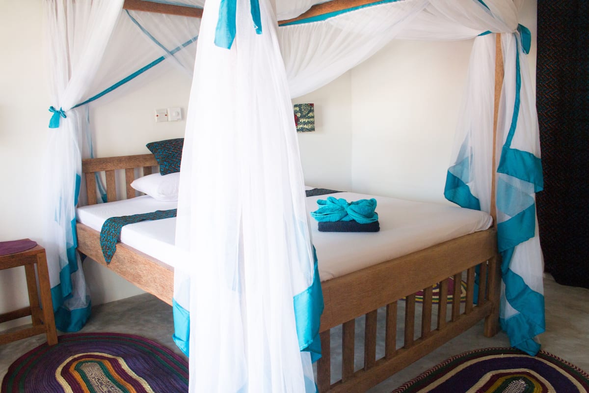 A single bed with a canopy, a small wooden stool, and a colorful rug.
