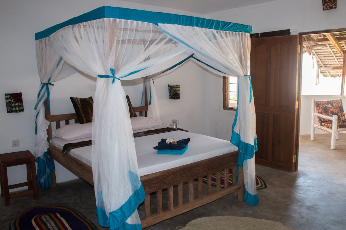 A bedroom with a four-poster bed, a small bedside table, and a chair.